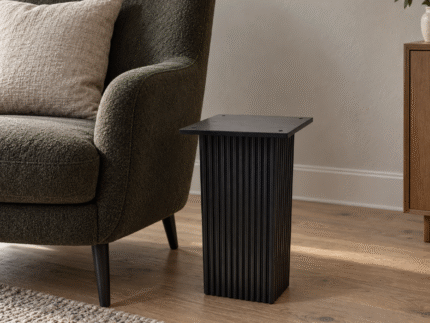 Black wooden carved base end table beside a lounge chair in a contemporary living room
