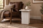 White wooden carved end table beside a leather lounge chair in a contemporary living room