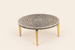 Round cocktail table with a black-and-ivory radial patterned top and gold-toned legs