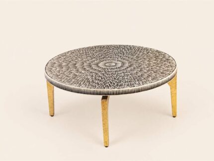 Round cocktail table with a black-and-ivory radial patterned top and gold-toned legs