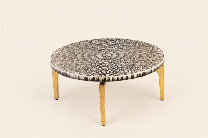 Round cocktail table with a black-and-ivory radial patterned top and gold-toned legs