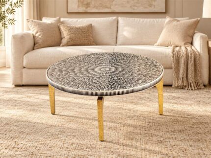 Round black-and-ivory patterned cocktail table with gold-toned legs in front of a cream sofa