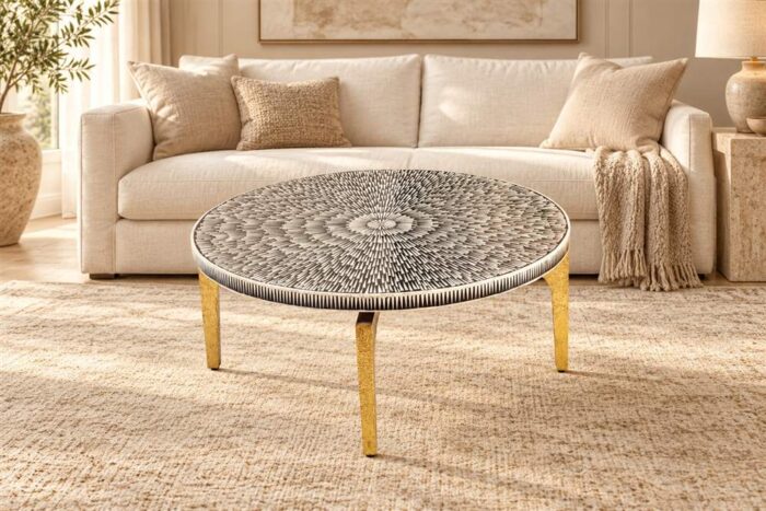 Round black-and-ivory patterned cocktail table with gold-toned legs in front of a cream sofa